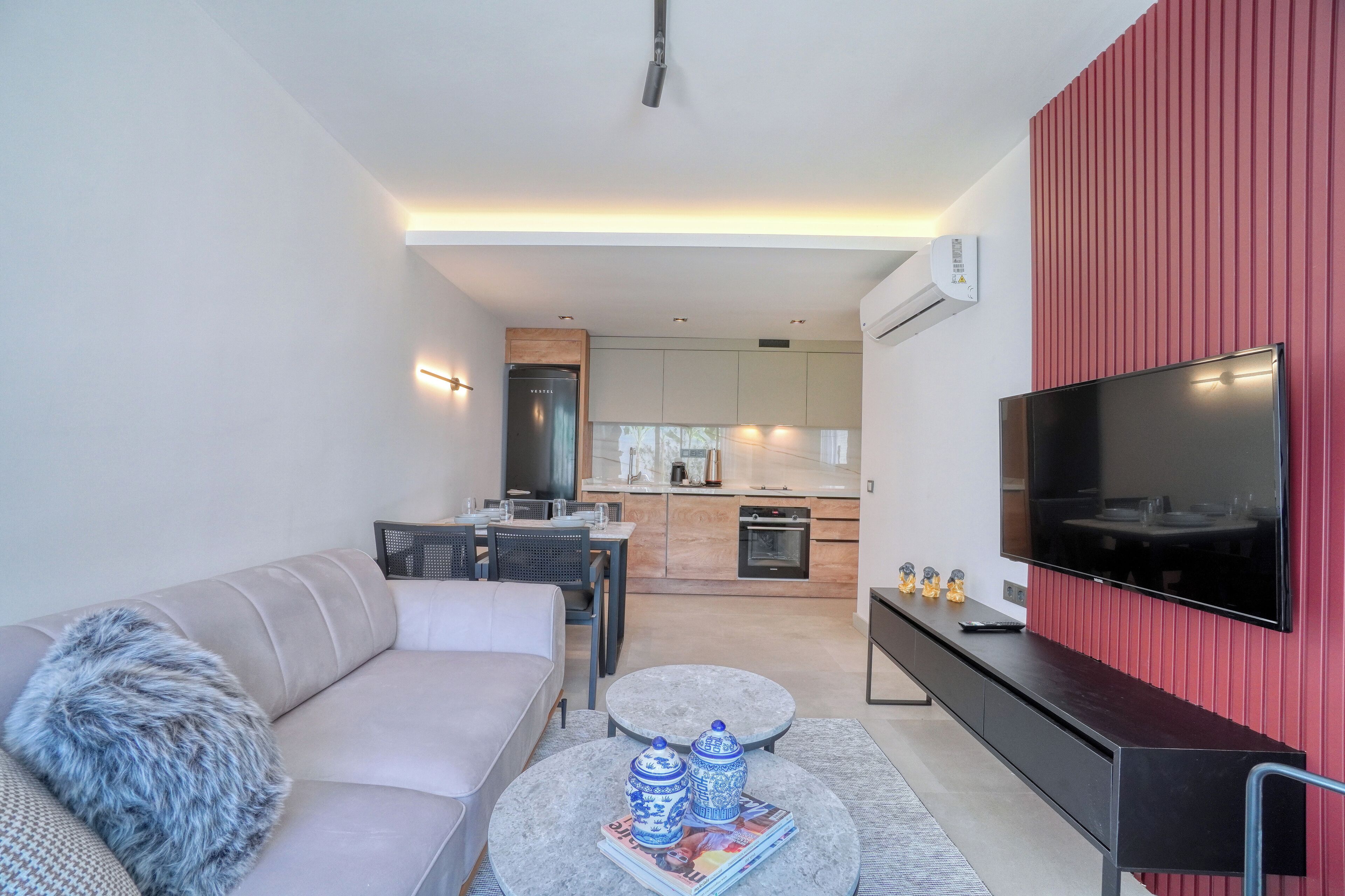 A modern living room with a sofa, coffee table, and a flat-screen TV mounted on a red wall.