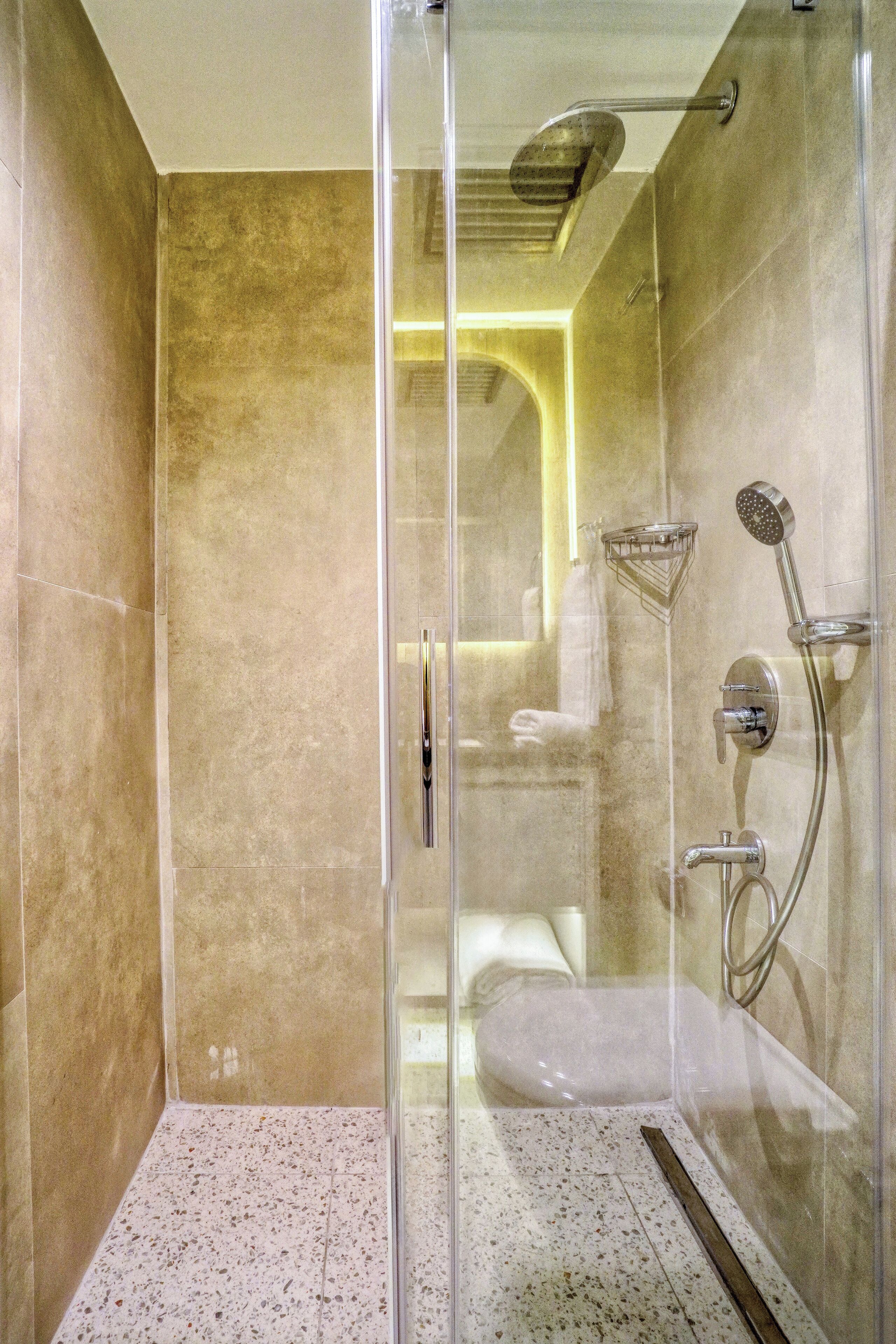 Eine moderne Dusche mit Glastür, Handbrause, Wandarmatur und Handtuchhalter.