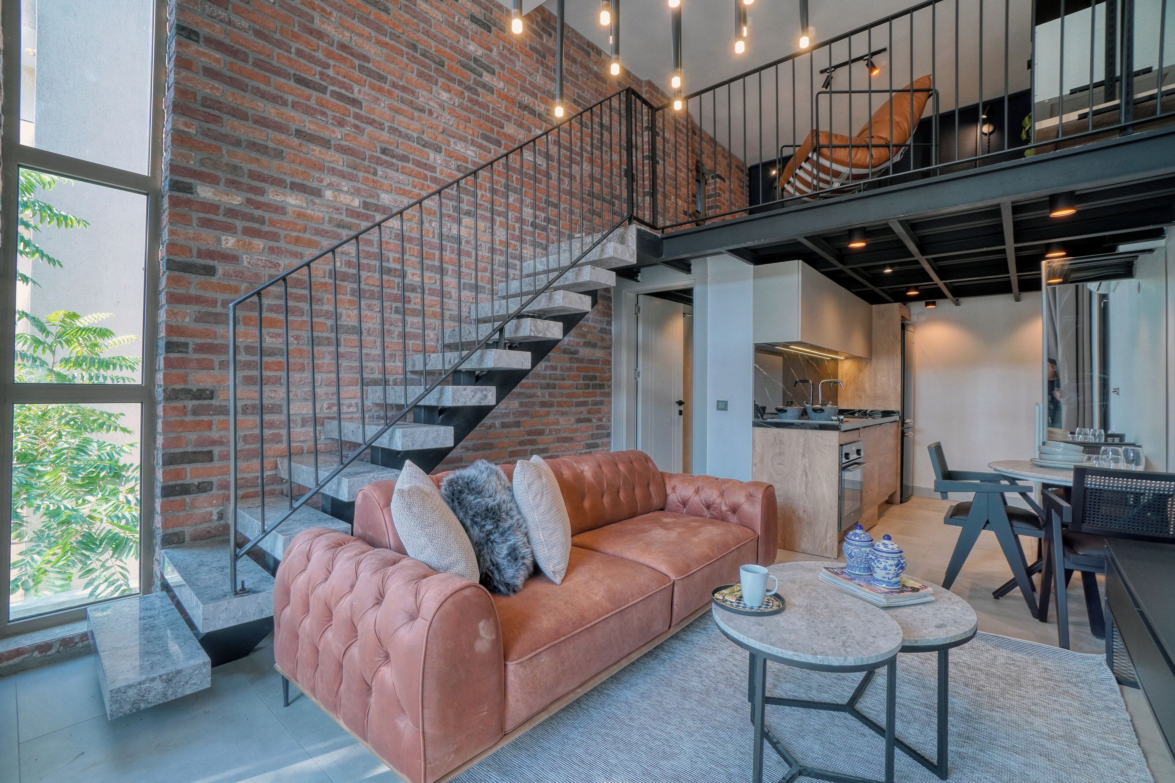 A spacious living area with a brick wall, a leather sofa, a dining table, and a staircase.