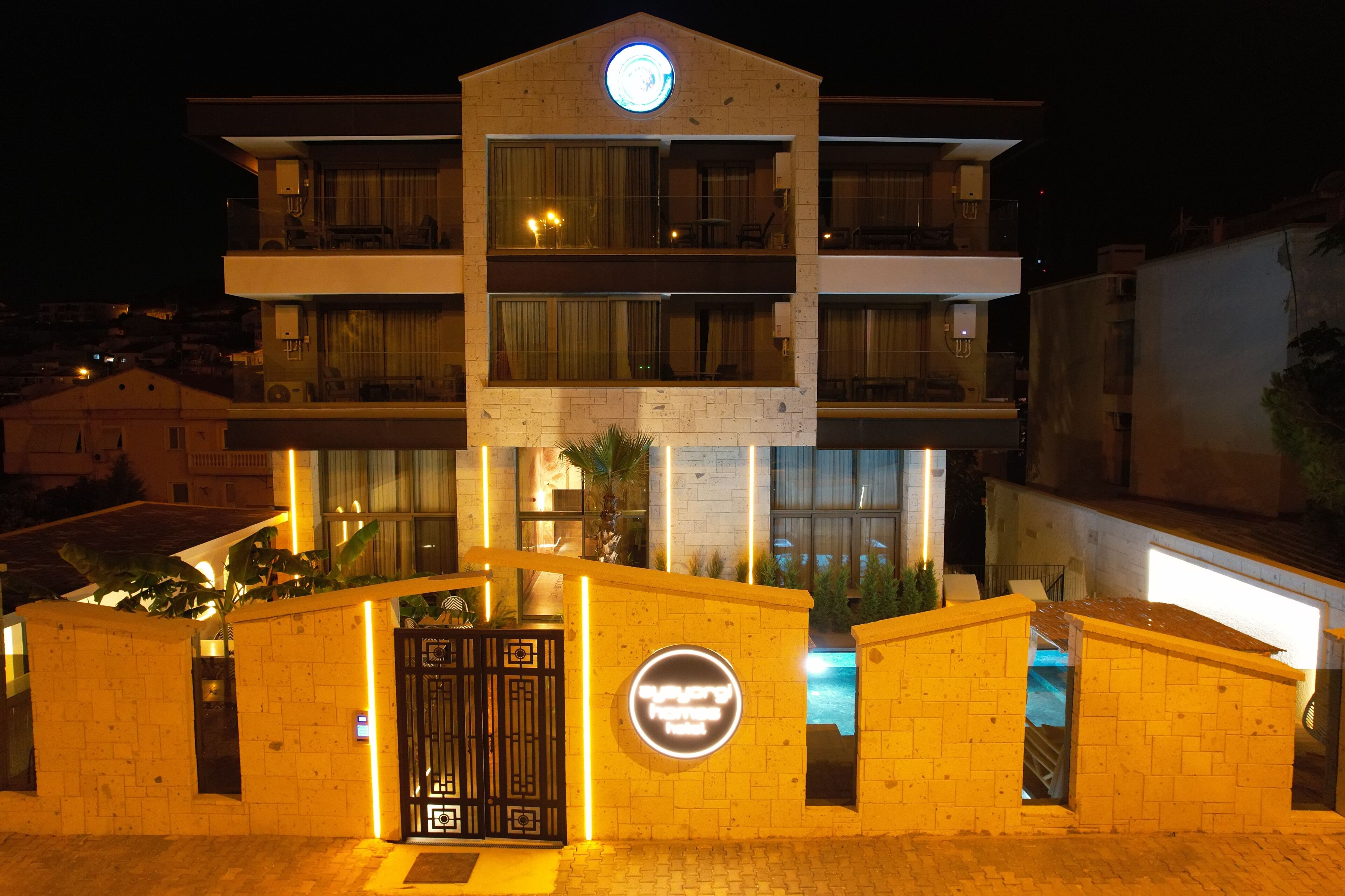 A multi-story hotel with a prominent circular sign on the facade, a gated entrance, and a visible pool area.