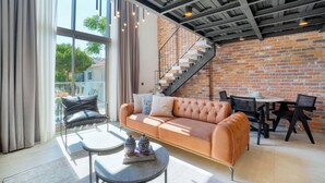 A modern living room with a leather sofa, a round coffee table, and a dining area with chairs and a table. A brick wall and a staircase are visible in the background. - Ayayorgi Homes & Suites (Cesme)