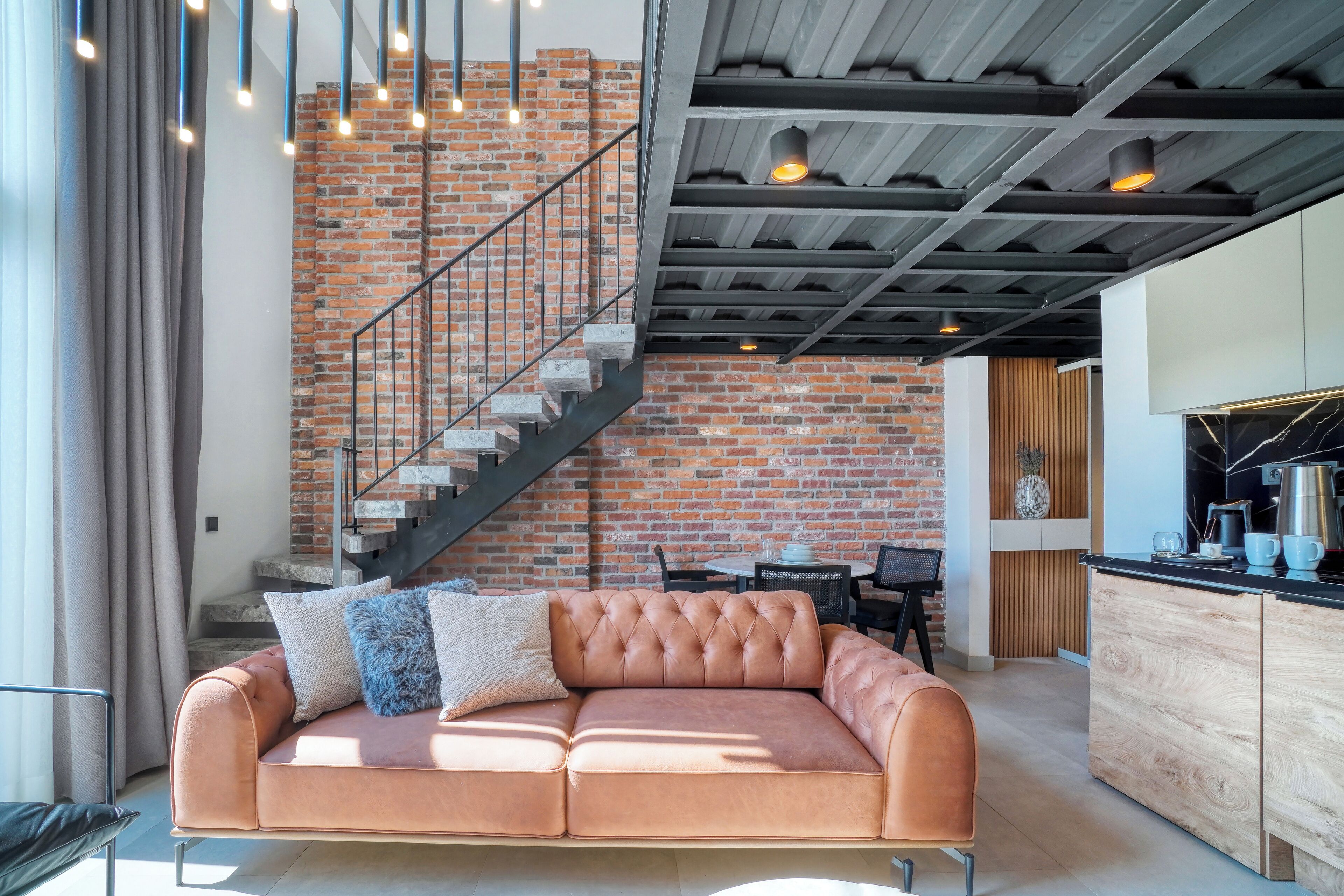 A modern living room with a leather sofa, a brick wall, and a staircase.