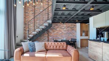 A modern living room with a leather sofa, a brick wall, and a staircase.