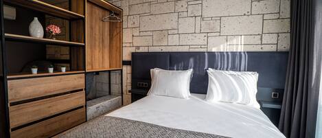 A modern hotel room with a brick-patterned wall, a large bed with white linens, a wooden dresser, and a hanging garment rack.