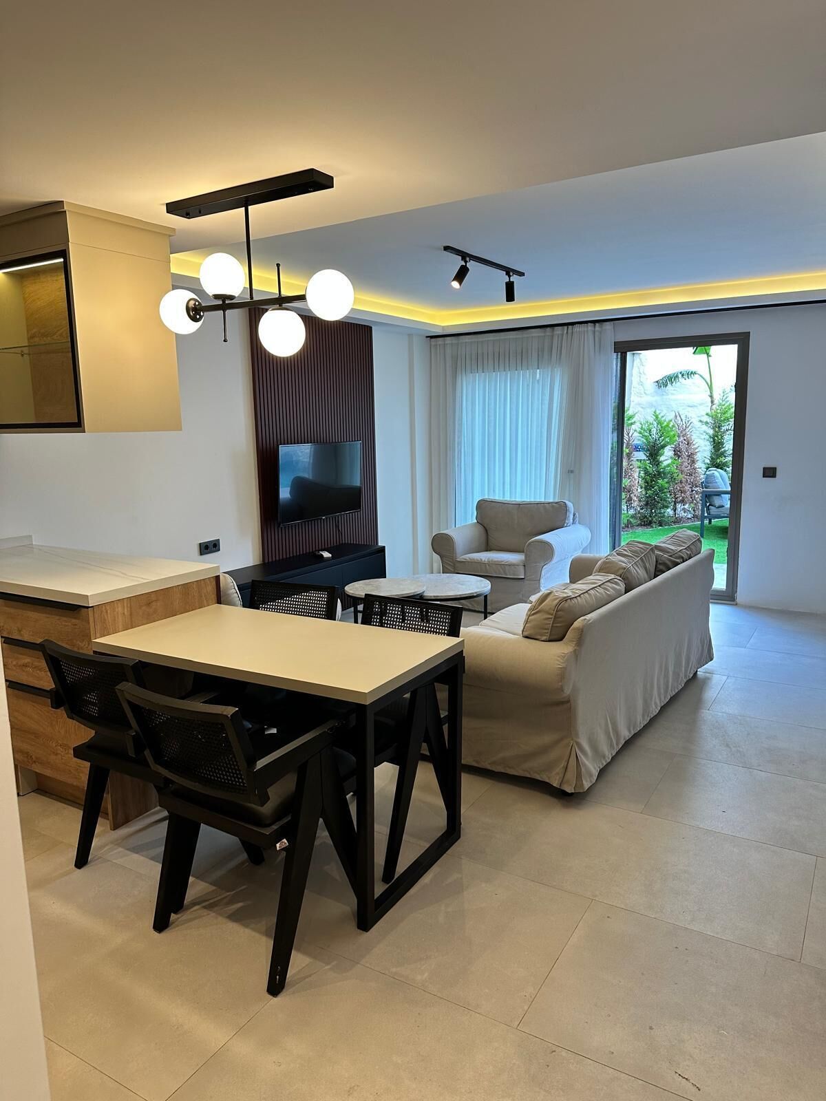 Een moderne woonkamer met een bank, een eettafel met stoelen, een flatscreen televisie en een keuken met een aanrecht en kastjes.