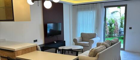 Een moderne woonkamer met een bank, een eettafel met stoelen, een flatscreen televisie en een keuken met een aanrecht en kastjes.