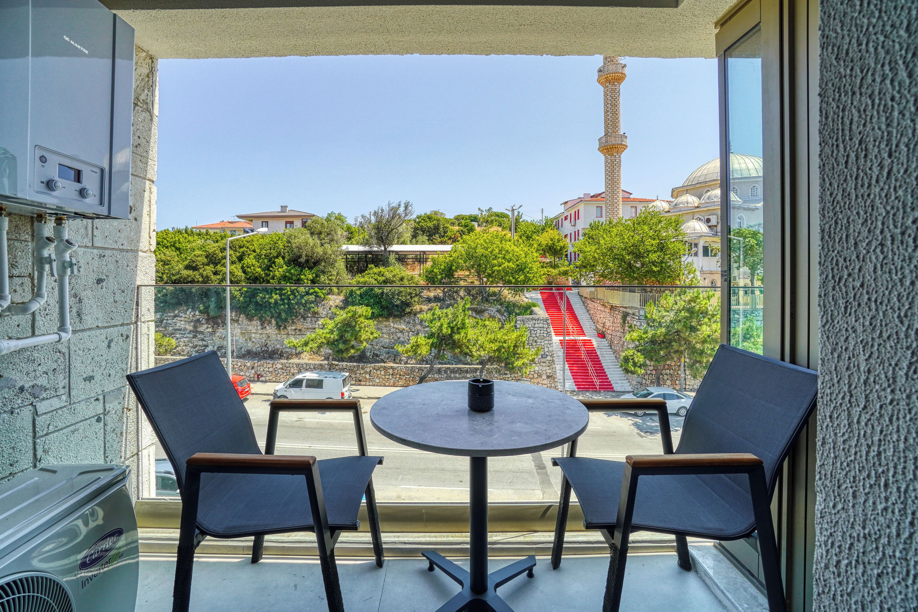A balcony with a table and chairs, overlooking a street with cars and a mosque with a minaret.