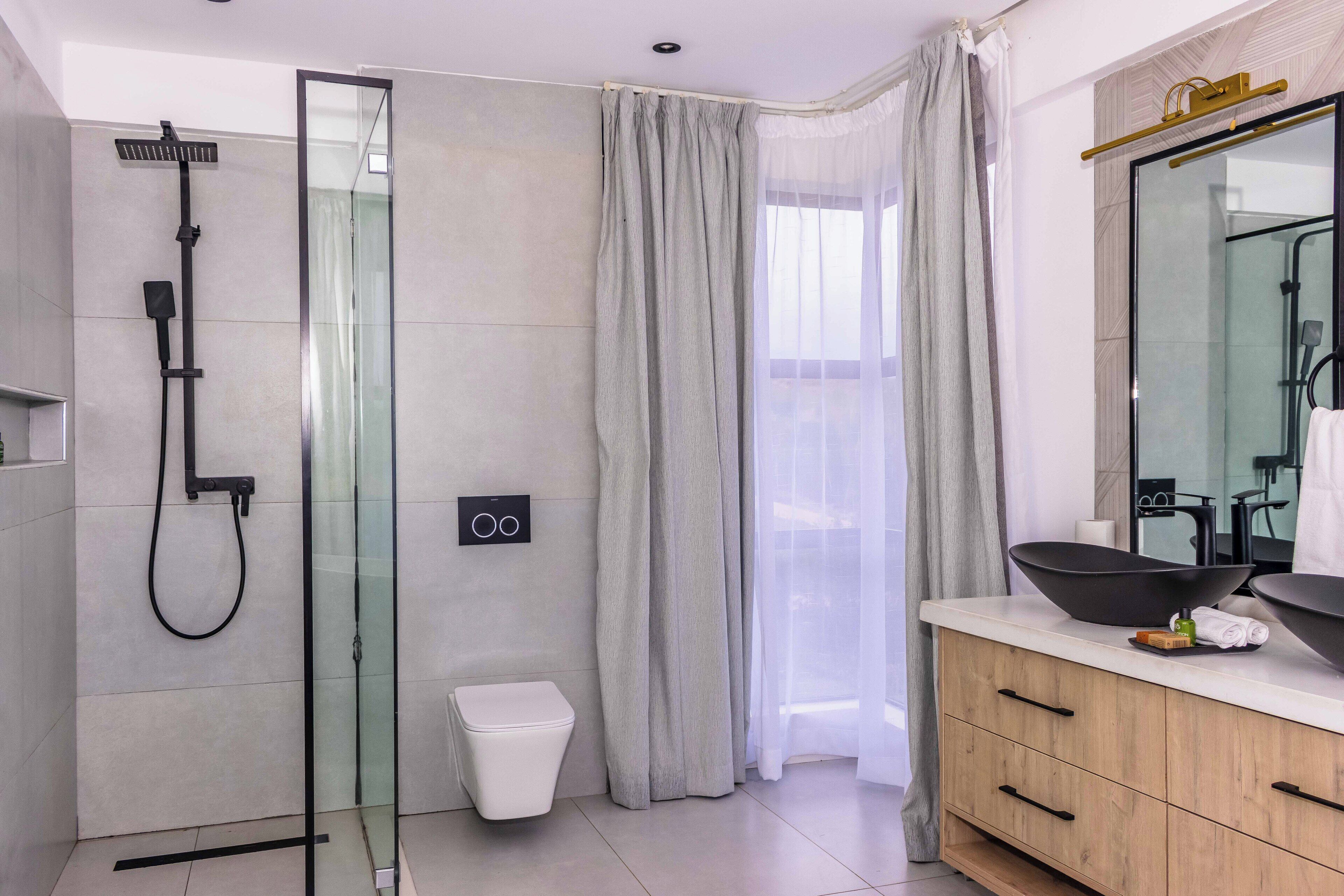 A modern bathroom with a glass shower enclosure, a toilet, and a vanity with a large mirror and a bowl sink.
