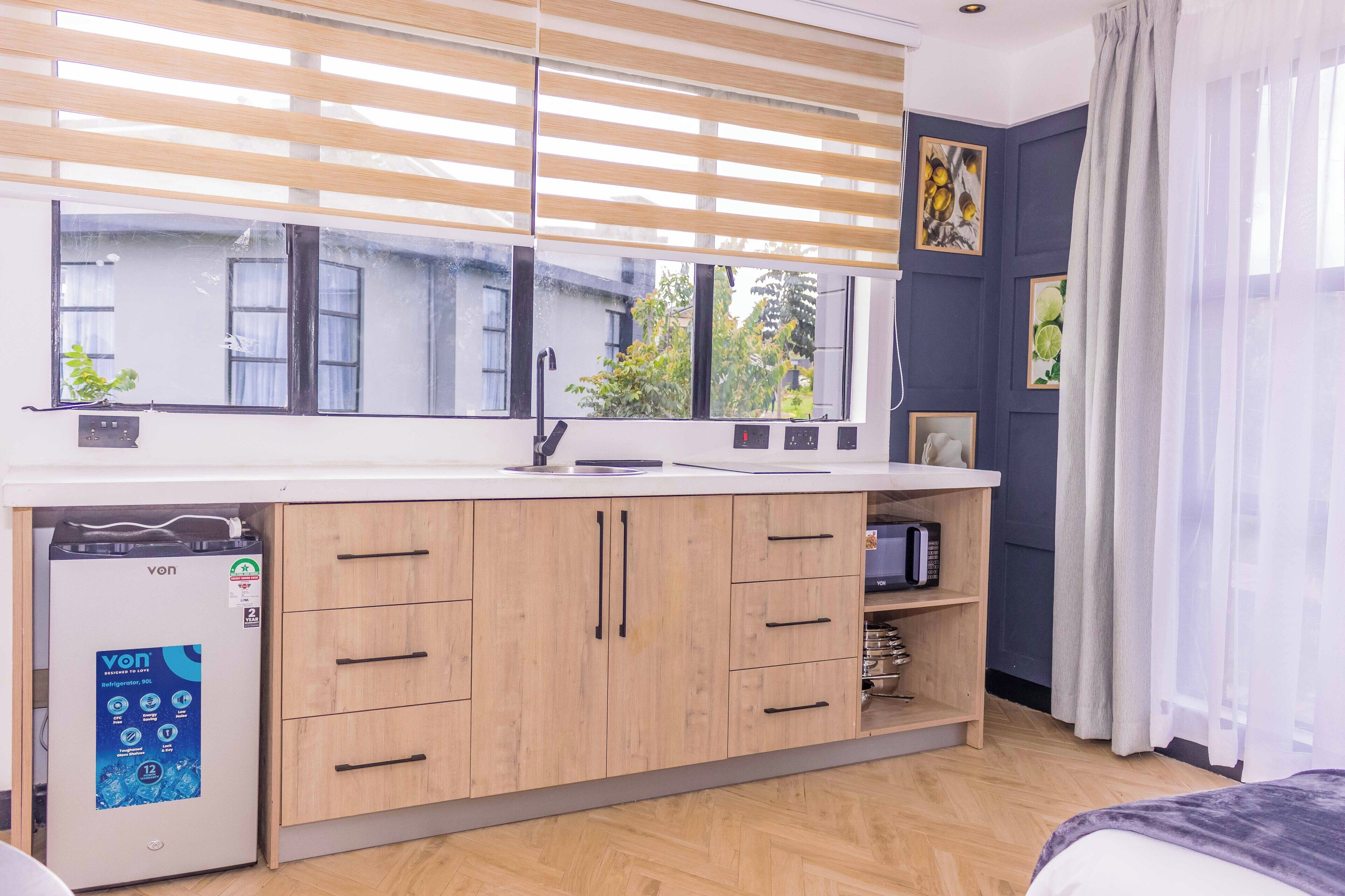 Une cuisine moderne avec des meubles en bois, un lave-vaisselle encastré et une grande fenêtre équipée de stores.