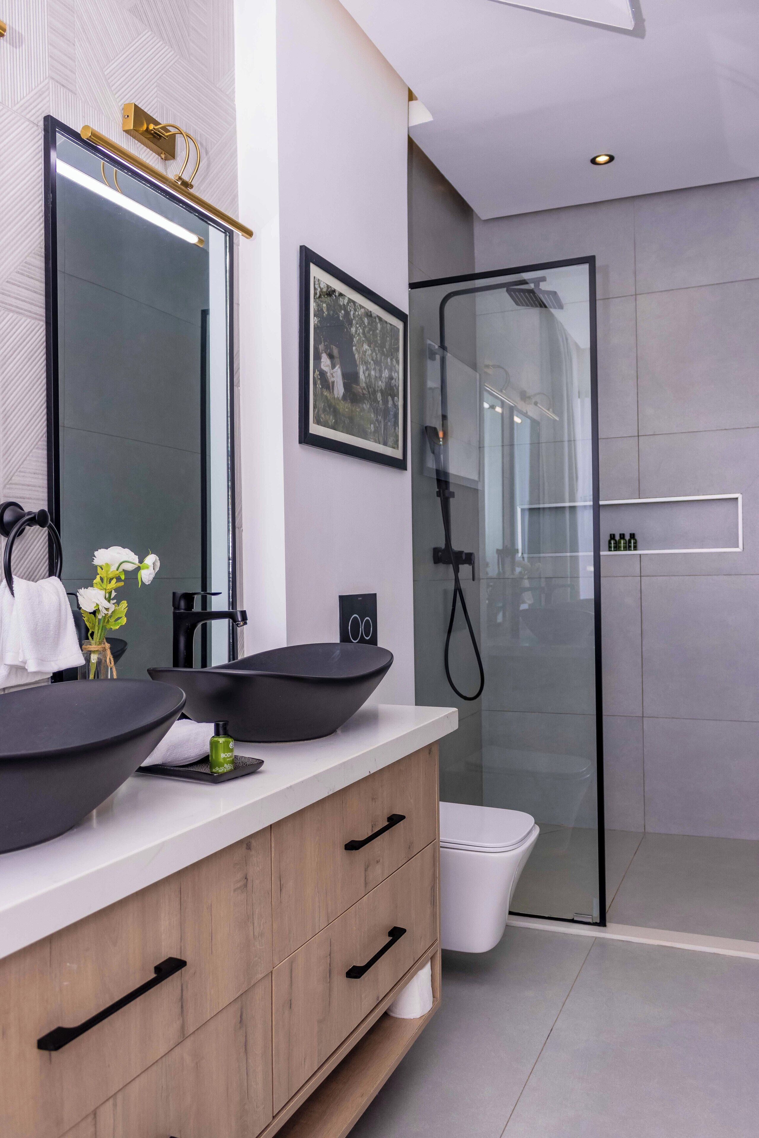 A modern bathroom with a large mirror, black vessel sinks, a glass shower enclosure, and a wooden vanity.