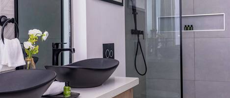 A modern bathroom with a large mirror, black vessel sinks, a glass shower enclosure, and a wooden vanity.