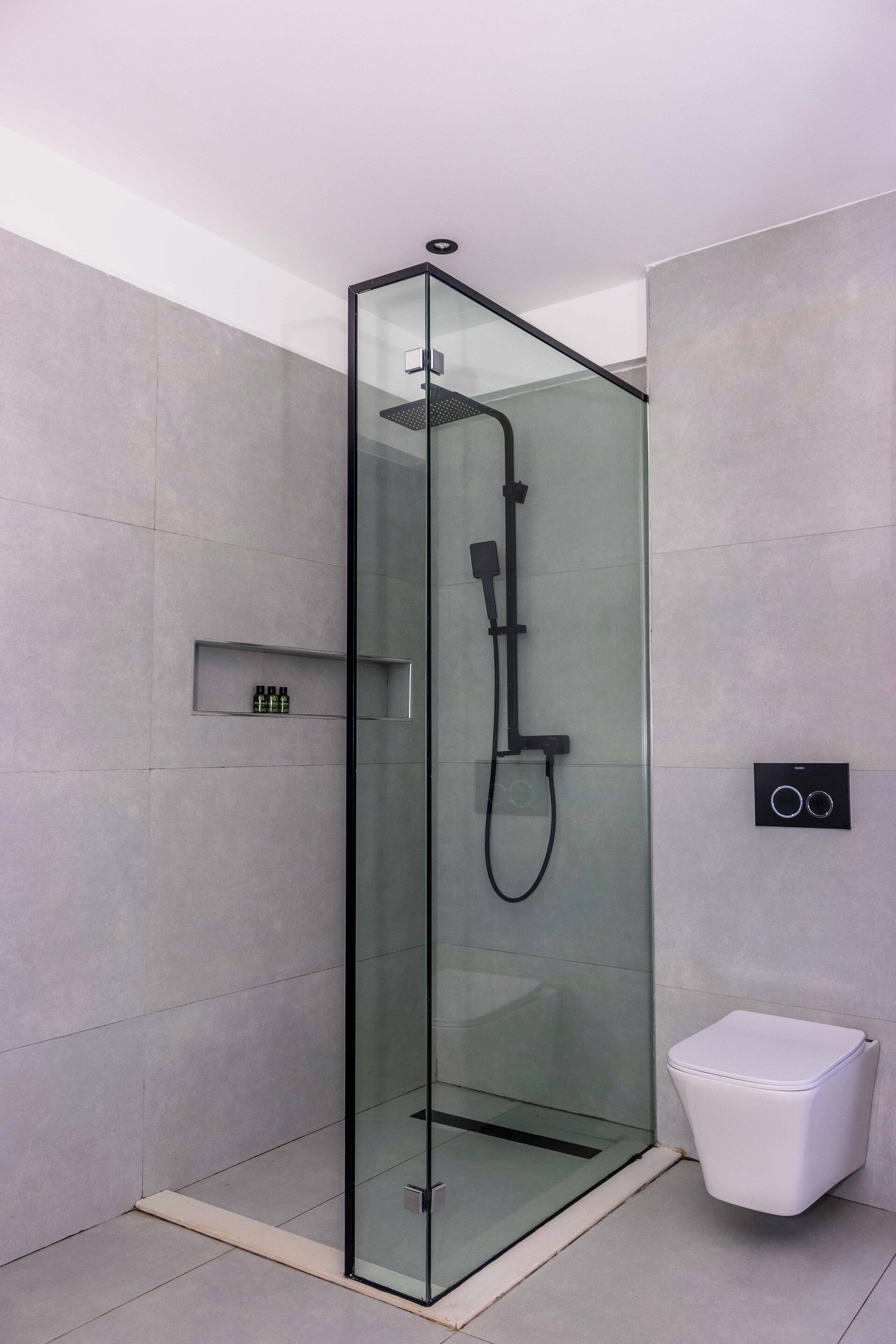 Box de chuveiro moderno com porta de vidro, chuveiro manual e painel de controle fixado na parede.