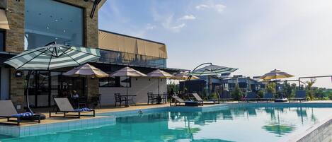 Una piscina al aire libre, sombrillas, sillones reclinables de piscina