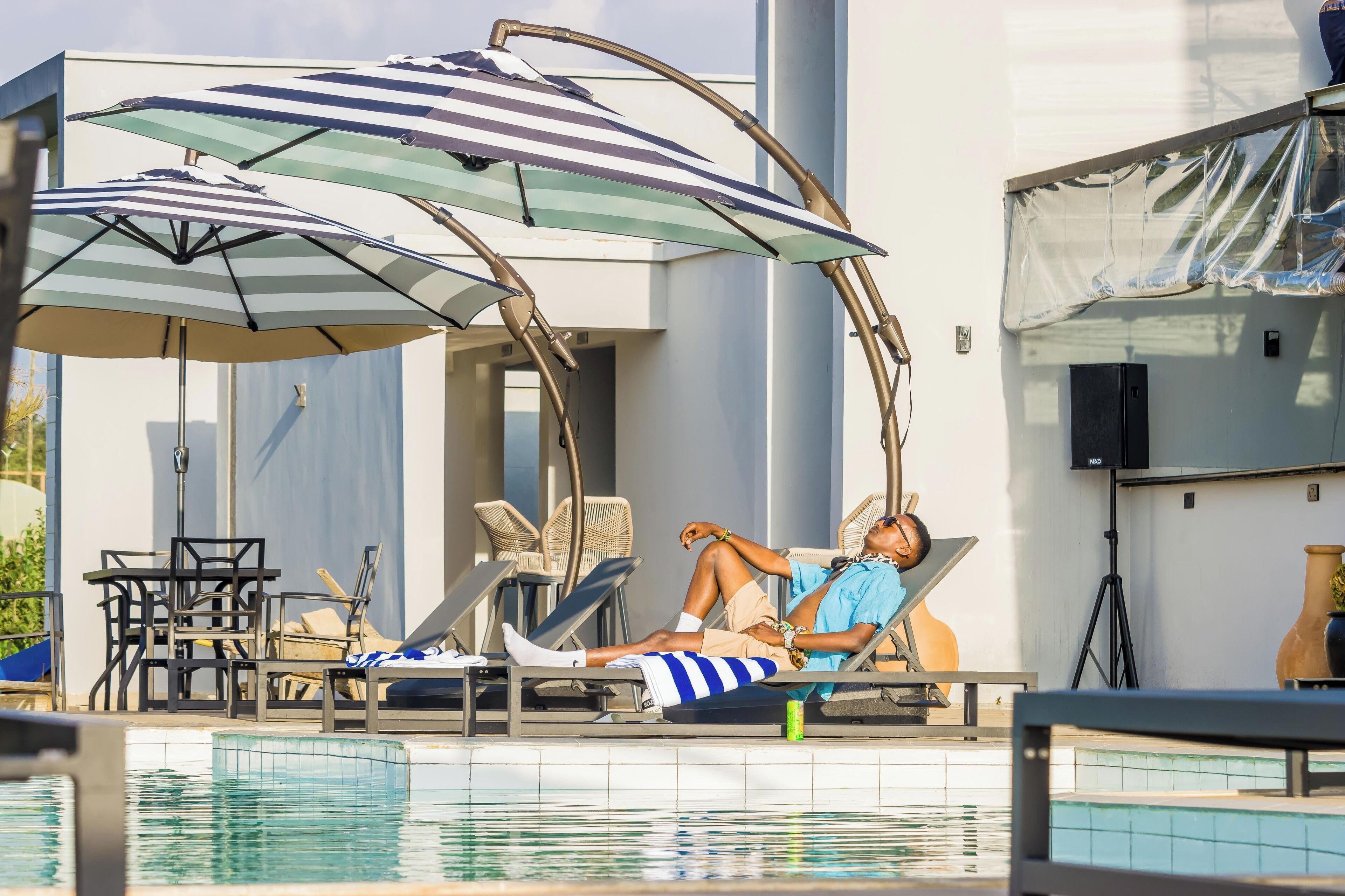 Ein Poolbereich mit Liegestühlen, gestreiften Sonnenschirmen und einem modernen Gebäudebau.