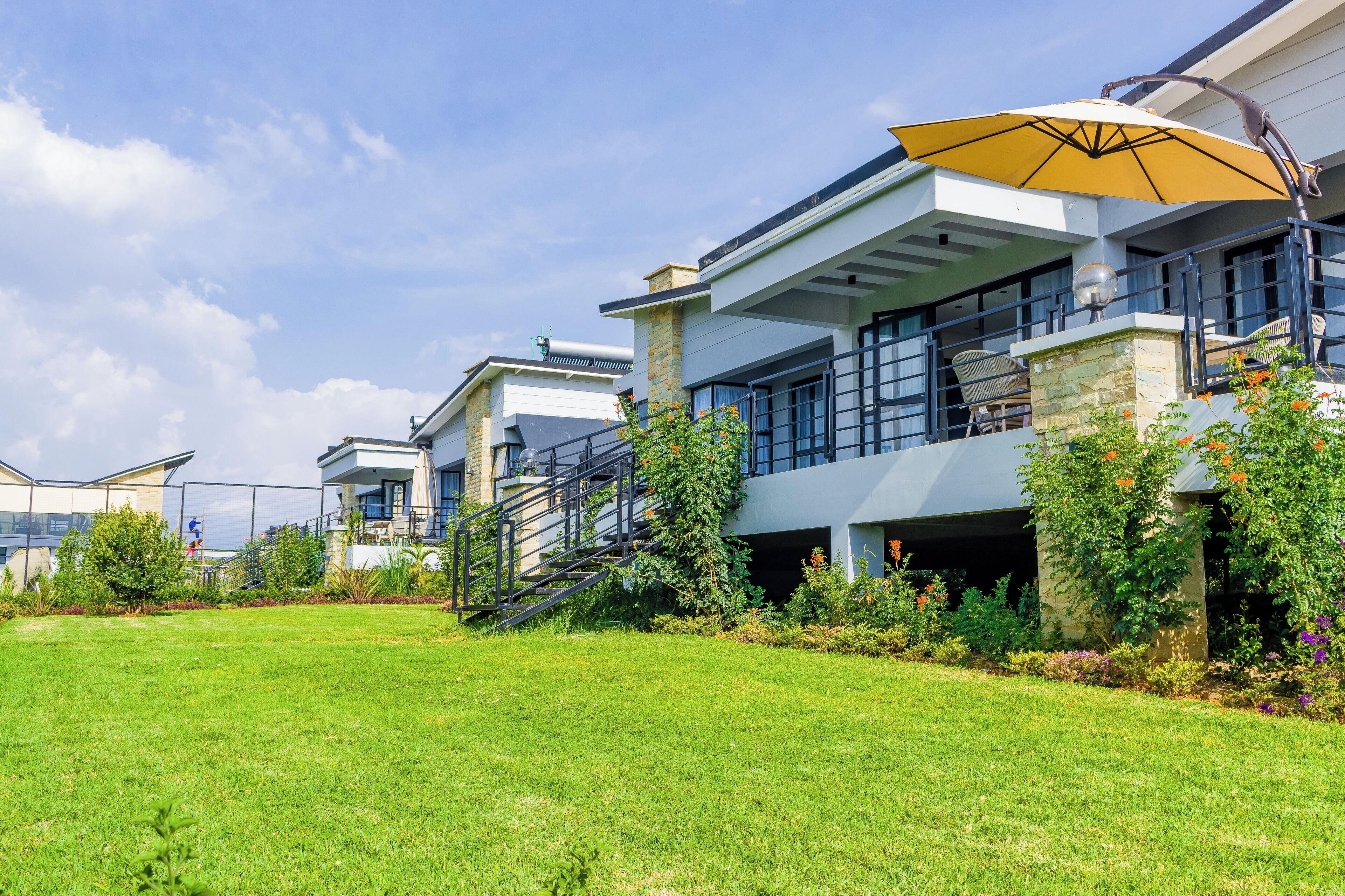 A modern residential building with a spacious lawn, outdoor seating area, and a large umbrella.
