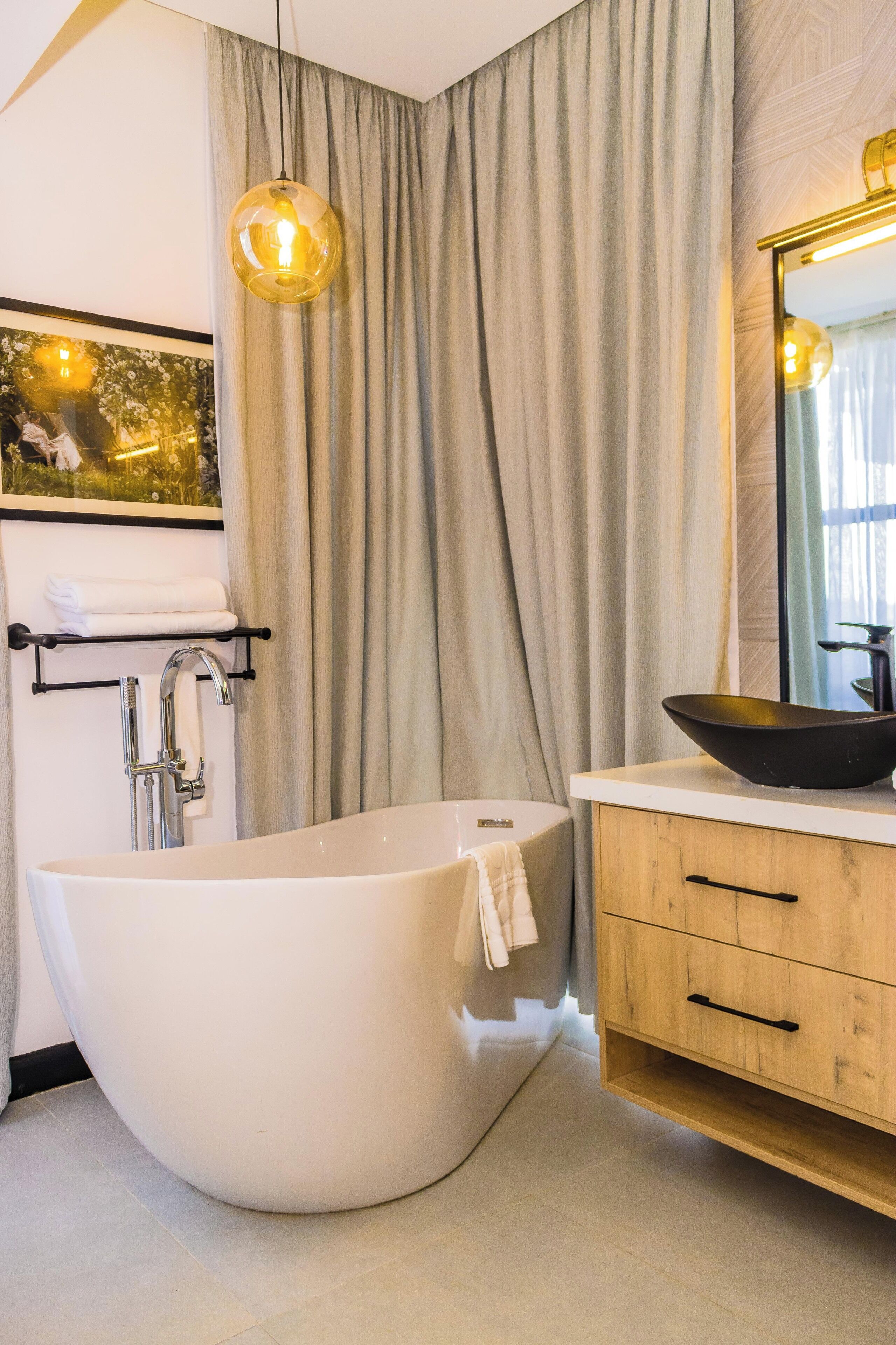 Ein modernes Badezimmer mit einer freistehenden Badewanne, einem Holzkosmetikschrank mit schwarzem Waschbecken und einem großen Spiegel.
