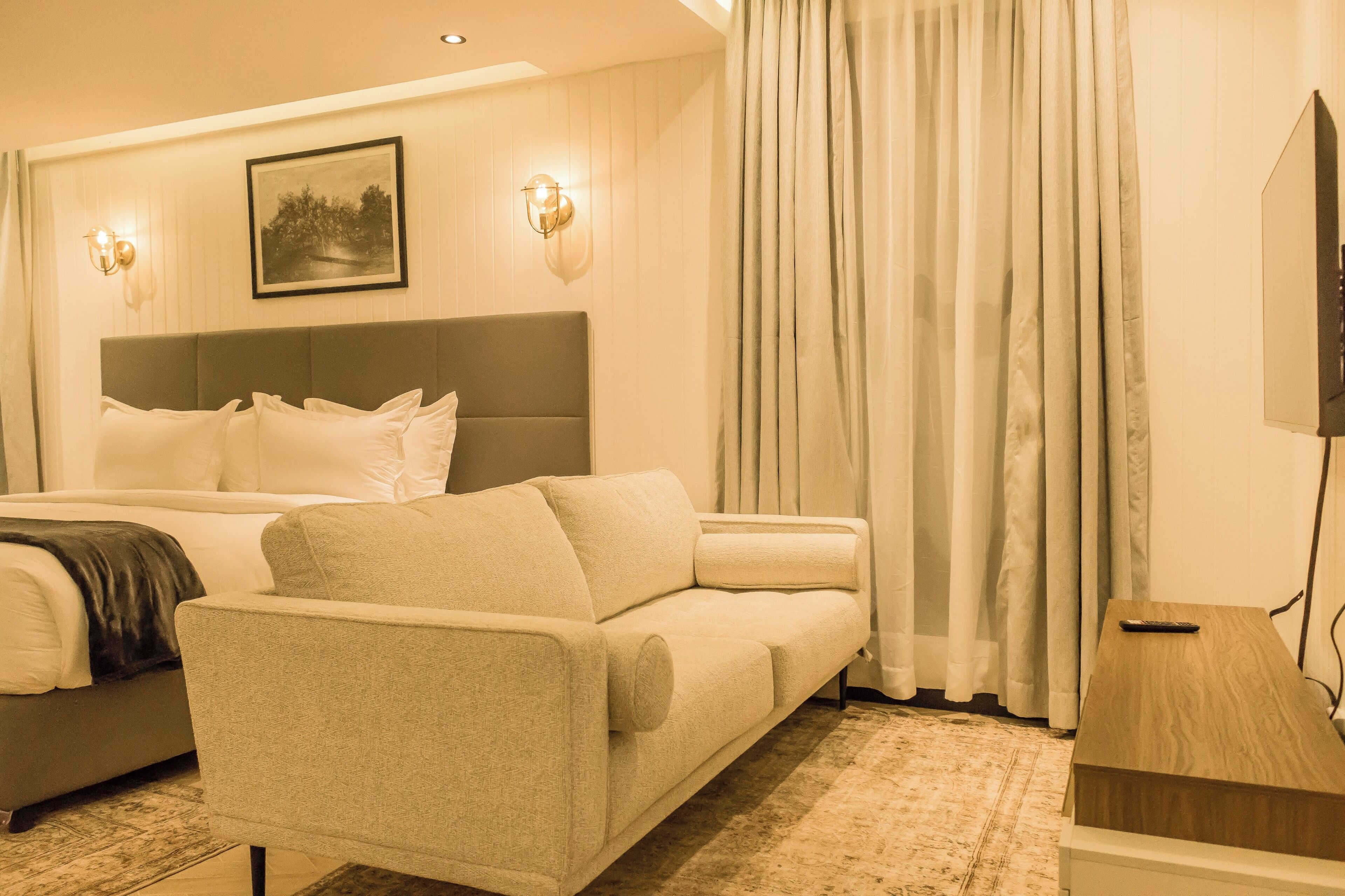 A hotel room with a bed, a sofa, a TV, and a painting on the wall.