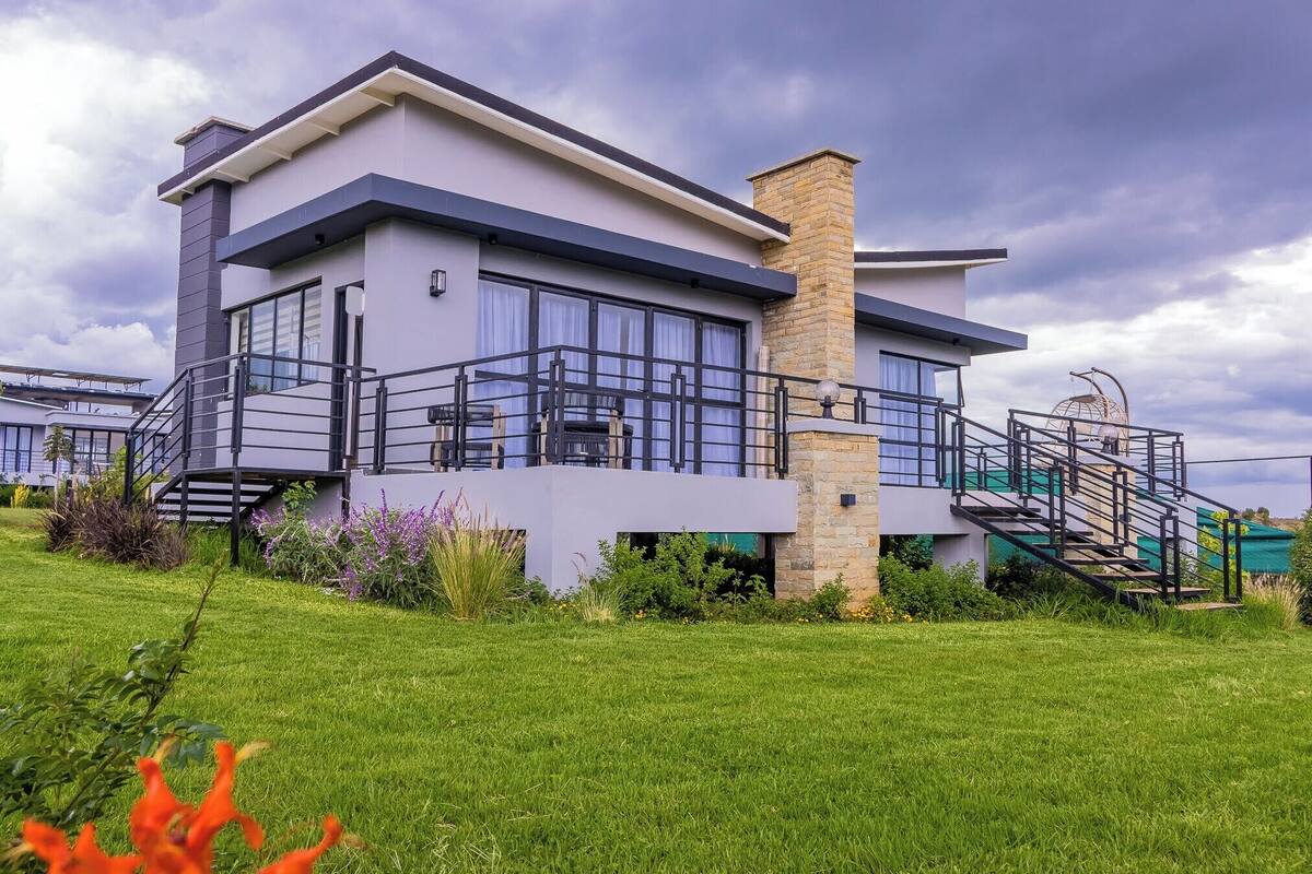 A modern two-story house with a balcony, a staircase, and a well-maintained lawn.
