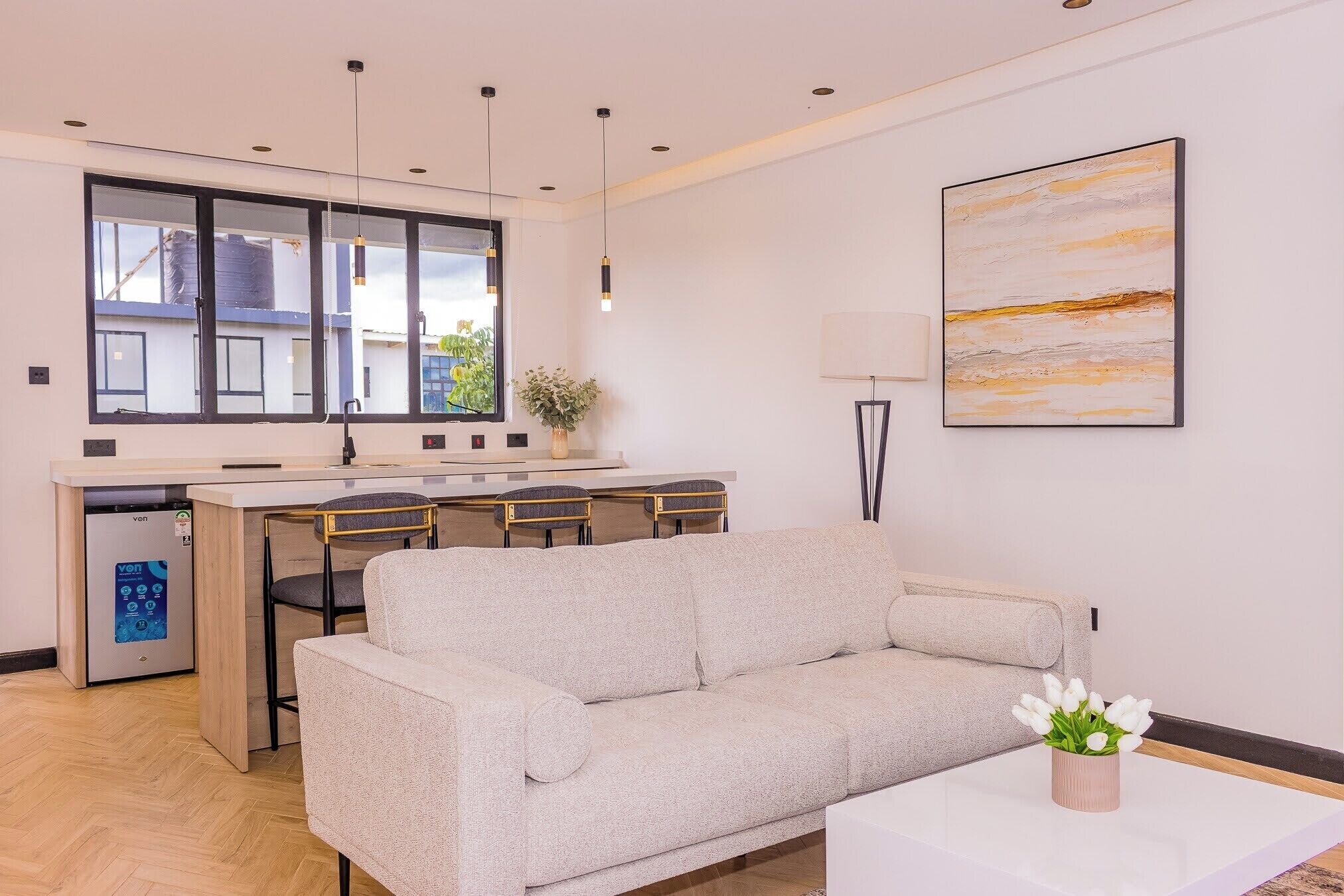 A modern living room with a sofa, a coffee table, and a dining area with chairs and a small kitchen.