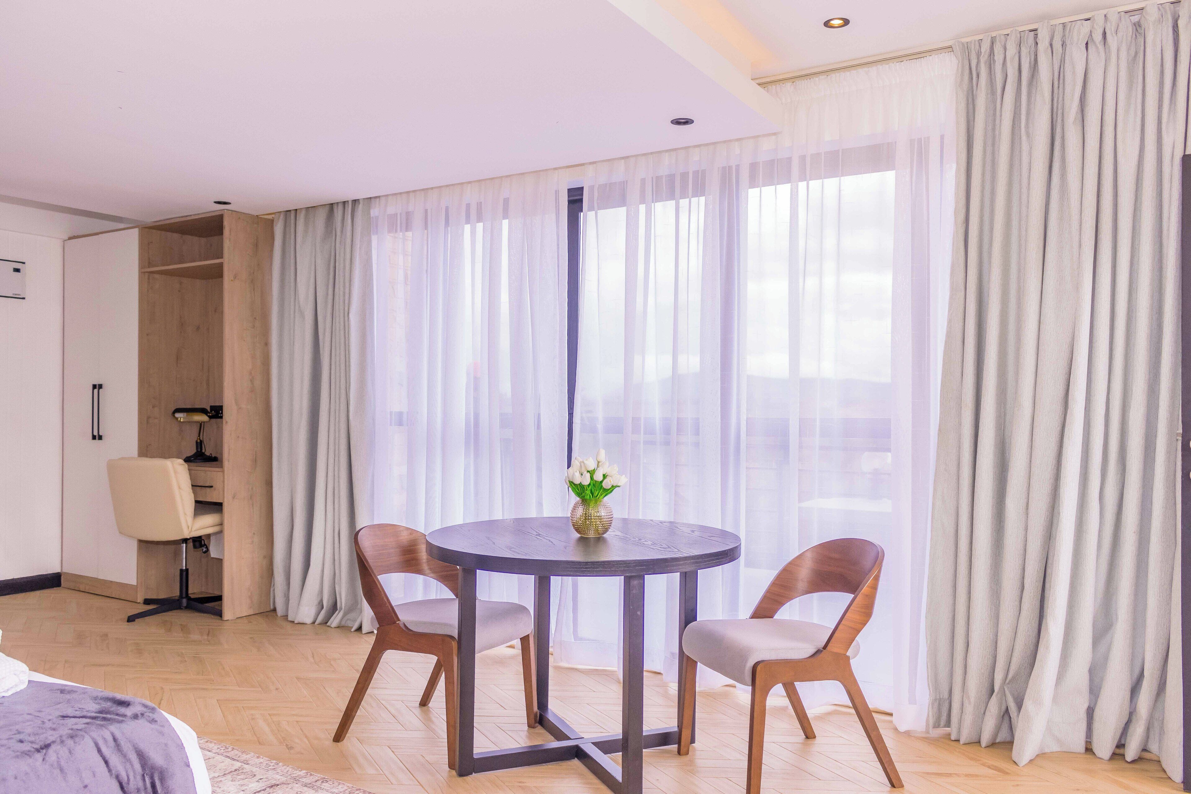 A hotel room with a round dining table, two chairs, a small desk with a chair, and a bed.