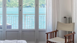 Una habitación con cama, una silla y vistas a un lago y montañas a través de amplios ventanales.