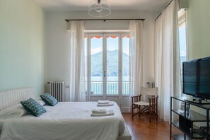 A bedroom with a bed, a TV, a chair, and a view of mountains and water. - Villa Helios in Menaggio (Menaggio)