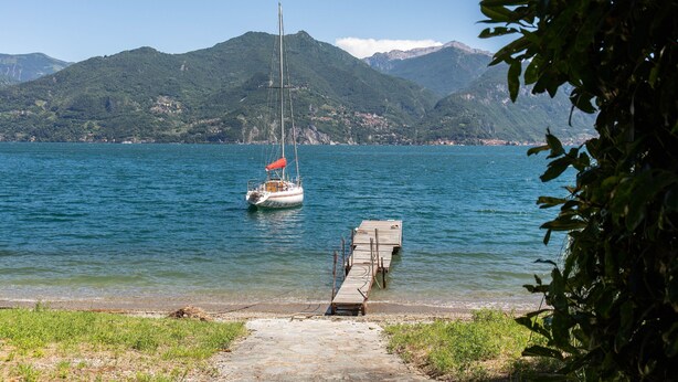Un lago tranquilo con un velero amarrado a un muelle de madera, rodeado de colinas verdes exuberantes.