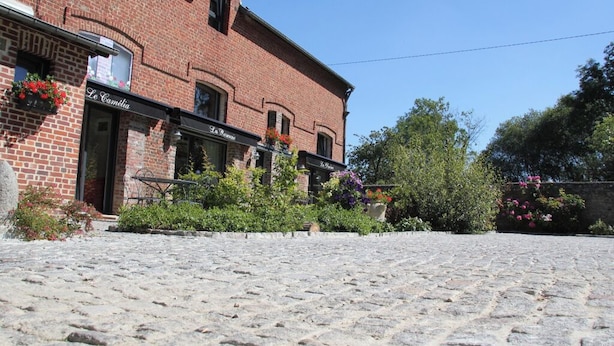 Une rue pavée bordée d’un bâtiment en briques où se trouvent les devantures de boutiques appelées « La Camélia » et « La Roseraie ».