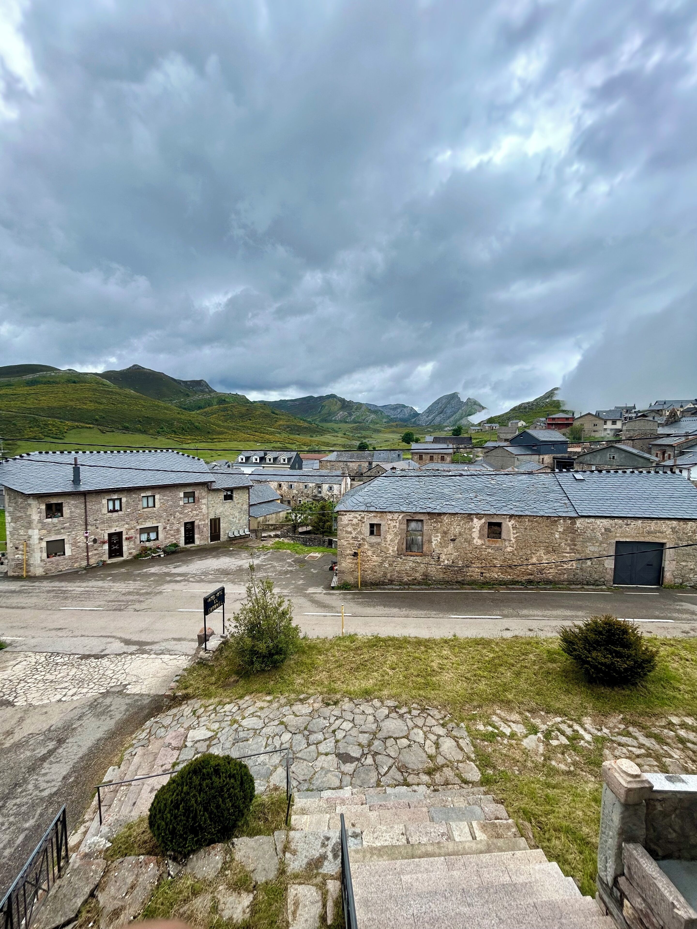 A stone building with a courtyard, surrounded by hills and a cloudy sky.