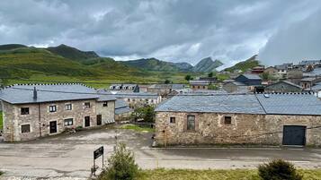 A stone building with a courtyard, surrounded by hills and a cloudy sky.