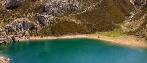 Un paisaje montañoso con un lago cristalino, terreno rocoso y vegetación escasa.