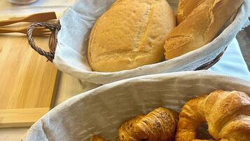 Une table sur laquelle on trouve des paniers de pain et de viennoiseries, des saladiers remplis de fruits et une pile d’assiettes.