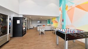 A modern indoor space with a foosball table, a vending machine, and a seating area with a sofa and chairs.