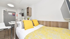 A hotel room with a bed, a desk, a chair, a small table, a mirror, and a TV.