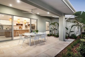 A modern kitchen with glass doors, a dining area with white chairs, and a ceiling fan. - The Indiana A Space to Relax (Dunsborough)