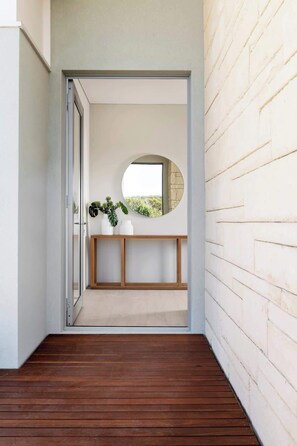 A hallway with a wooden floor, a white brick wall, a round mirror, and a wooden console table with plants.