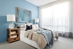 A bedroom with a bed, two bedside lamps, a nightstand with storage, a large abstract painting, and sheer curtains. - The Indiana A Space to Relax (Dunsborough)