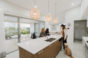 A modern kitchen with a large island, pendant lights, and a view to the outside.