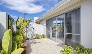 A modern house with a patio, large windows, and tropical plants.