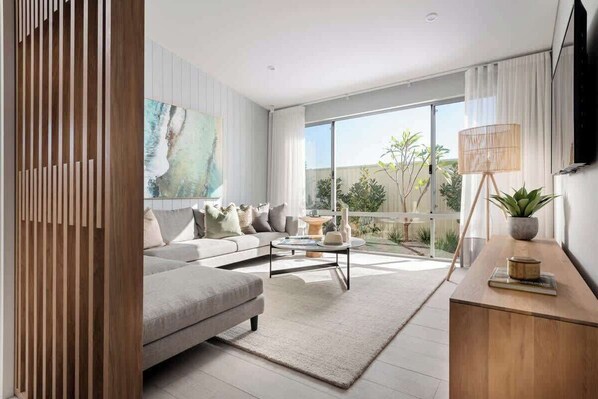 A modern living room with a sofa, coffee table, and a large window with a view of greenery.