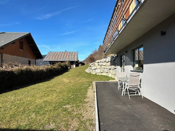 A modern building with a stone wall, a grassy area, and a patio with chairs. - The Haven, Montriond, garden, 2/4 persons (Montriond)