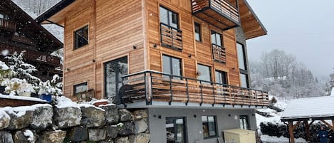 Una cabaña de madera de varios pisos con un balcón, base de pared de piedra y un espacio de estar al aire libre cubierto.