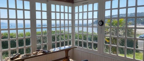 A room with large windows, a wooden bench, and a table with various items.