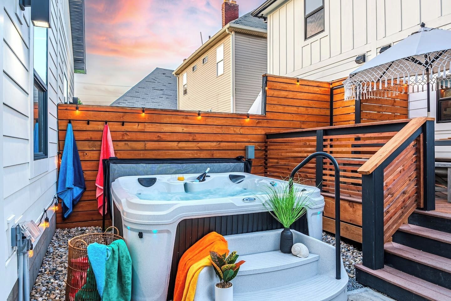 A hot tub in a backyard with wooden fencing, a staircase, and a potted plant.