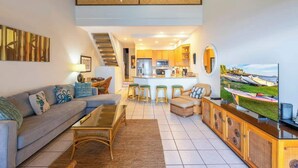 A modern living room with a sofa, coffee table, and a TV displaying a scenic view. - Oceanfront spacious 2 bedroom condo, updated, private beach, walkable area (Napili-Honokowai)