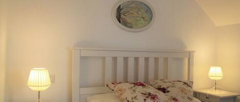 A bedroom with a white headboard, two bedside lamps, a floral pillow, and a round painting on the wall.