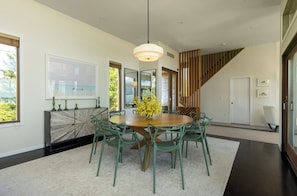 A modern dining room with a round table, green chairs, and a central vase of yellow flowers.