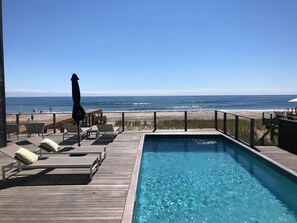 Een houten terras met ligstoelen en een zwembad met uitzicht op een strand.
