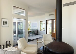A modern living room with a fireplace, a dining area with a table and chairs, and a large window providing natural light.