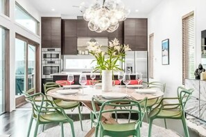 Een moderne eetruimte met een ronde tafel voor zes personen, omringd door groene stoelen. Op tafel staat een vaas met witte bloemen.